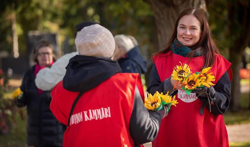 Ihmisiä Mummon Kammari -liiveissä. Hymyilevä Maria Vuoristo jakaa kukkia.