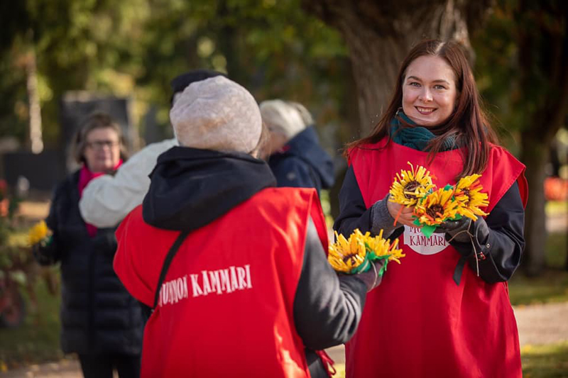 Ihmisiä Mummon Kammari -liiveissä. Hymyilevä Maria Vuoristo jakaa kukkia.