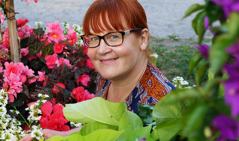 Hymyilevä nainen kukkien keskellä.