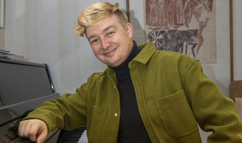 Hymyilevä mies nojaa pianoon.