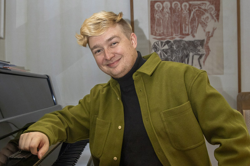 Hymyilevä mies nojaa pianoon.