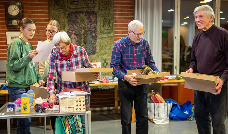 Kaksi ihmistä tutkii paperia, yksi nostaa jotain pöydältä pahvilaatikko toisessa kädessään, ja kaksi pitelee laatikoita käsissään.