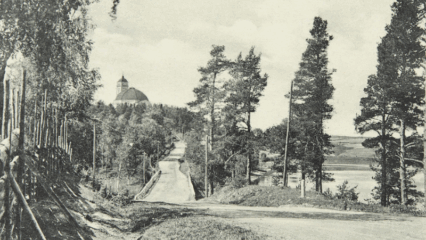 Vanha kuva, jossa näkyy tietä, metsää ja horisontissa kirkko.