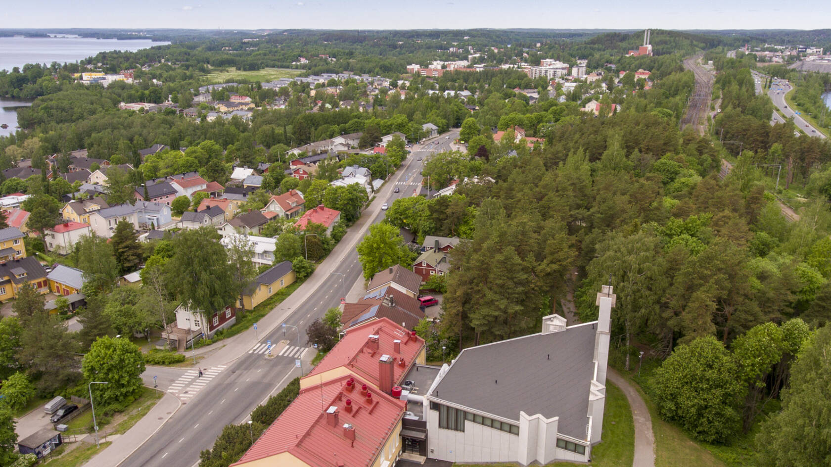 Ilmakuva kaupungista, jossa on vihreitä puistoja, asuinrakennuksia ja teollisuusrakennuksia järven rannalla.