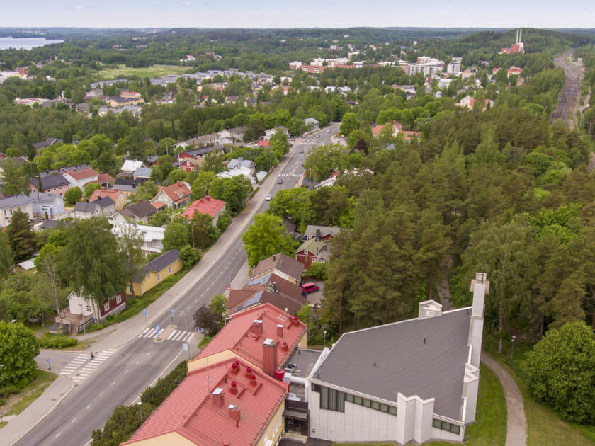 Ilmakuva kaupungista, jossa on vihreitä puistoja, asuinrakennuksia ja teollisuusrakennuksia järven rannalla.