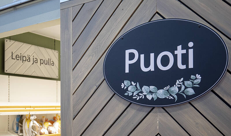 Puoti kyltti oven vieressä. Ovesta näkyy hyllyt, missä leipää.