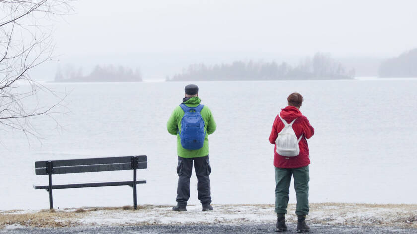 Kolme ihmistä seisoo harmaana talvipäivänä autiossa maisemassa ja katselee jäätynyttä järveä.