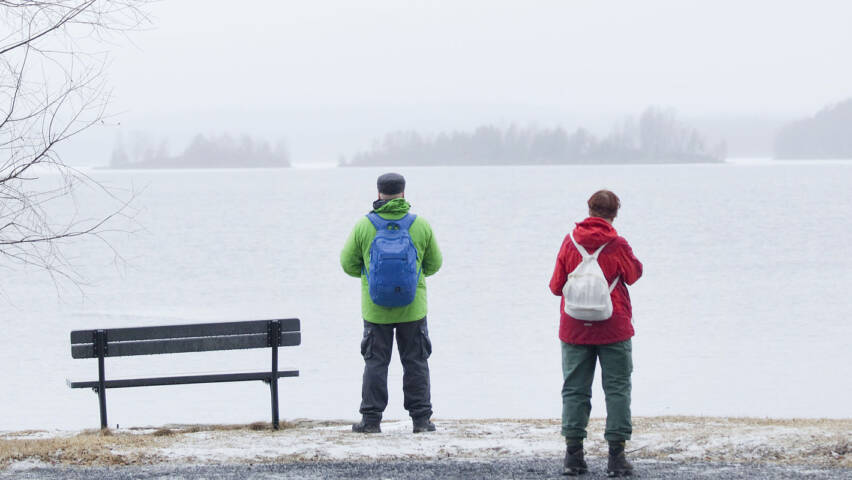 Kolme ihmistä seisoo harmaana talvipäivänä autiossa maisemassa ja katselee jäätynyttä järveä.