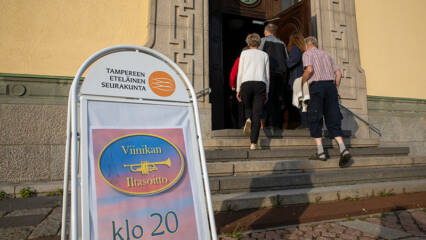 Ihmiset ovat kävelemässä kirkon pääoven rappusilla kirkkoon. Rappusien alla on iso kyltti jossa lukee viinikan iltasoitto klo 20.