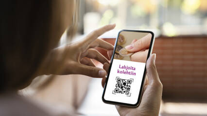 Matkapuhelin on kädessä ja puhelimessa näkyy QR-koodi.