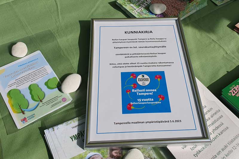 Kunnia kirja pöydällä,,ossa lukee: Reilun kaupan kaupunki Tampere ja Reilu kauppa ry myönsi huomionosoituksen Tampereen seurakunnille sinnikkäästä ja pitkäjänteisestä Reilun kaupan paikallisesta edistämistyöstä.