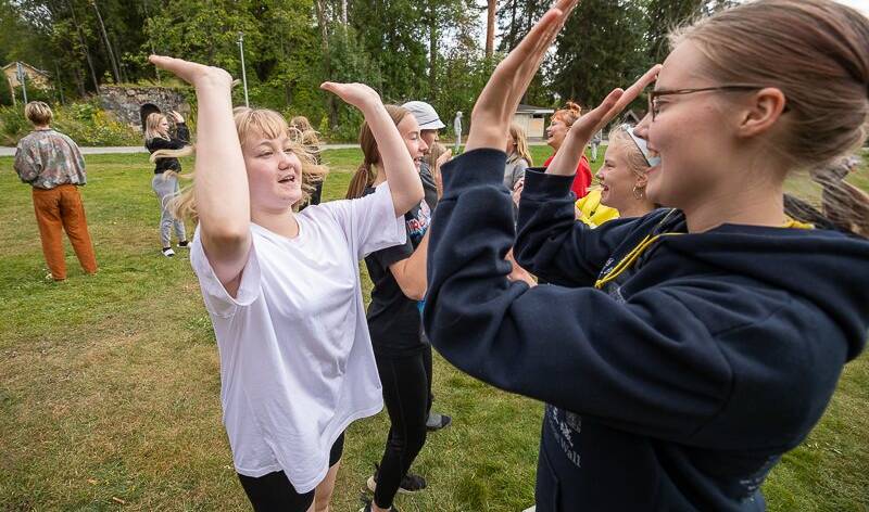 Nuoria rivissä kesäisellä kentällä,jossa he läpsyttävät käsiä yhteen ylhäällä.