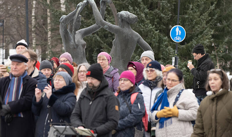 Iso joukko ihmisiä patsaan edessä, heistä osa rukoilee ja joku ottaa kuvia matkapuhelimella.
