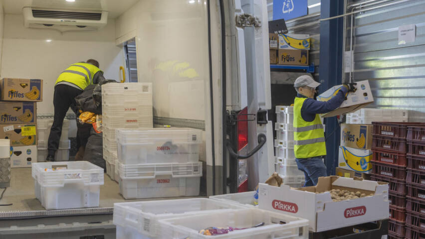 Kaksi henkilöä purkamassa ruokatarvikkeita autosta.