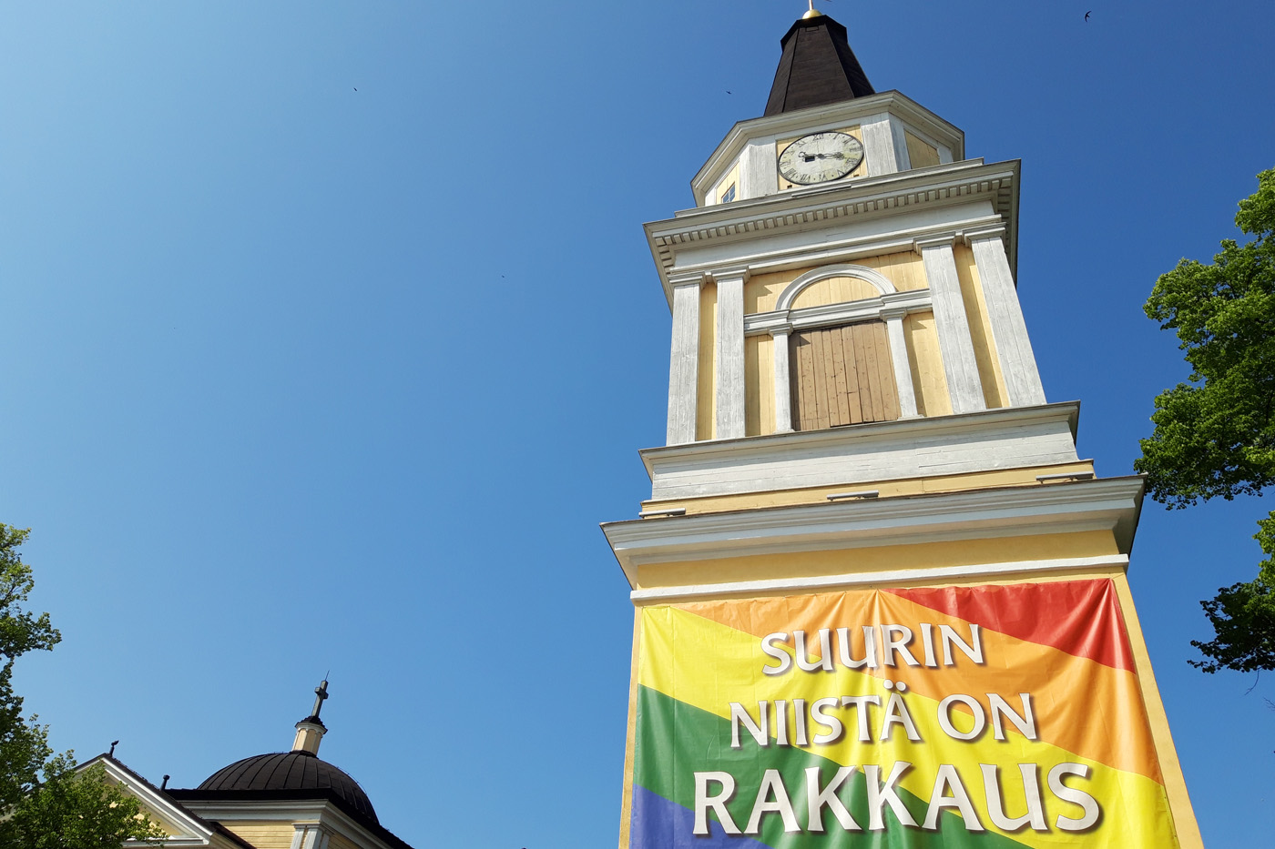 Tampereen Vanhan kirkon kellotapulissa banderolli sateenkaaren väreissä. Banderollissa lukee teksti: Suurin niistä on rakkaus.