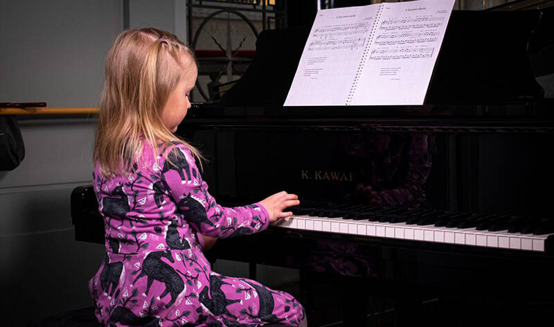Violettimekkoinen tyttö soittaa mustaa flyygeliä ja on kameraan selin.