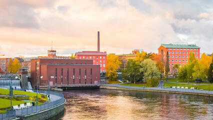 Tampereen koskipuisto syksyn väreissä. Nurmialueet ovat vihreät, mutta puiden lehdissä on havaittavissa keltaisuutta. Vesi virtaa Tampereel vesivoimalan lävitse.