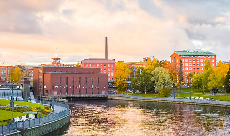 Tampereen koskipuisto syksyn väreissä. Nurmialueet ovat vihreät, mutta puiden lehdissä on havaittavissa keltaisuutta. Vesi virtaa Tampereel vesivoimalan lävitse.