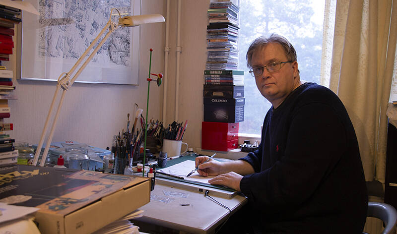 Graafikko ja sarjakuvapiirtäjä Tero Mattilan työpöydällä on useita purkkeja täynnä erilaisia piirustusvälineitä. Hänellä on mustekynä kädessään ja hän on kääntynyt katsomaan kuvaajaa kohti – hänellä on yhä keskittynyt ilme. On talvipäivä ja aurinko valaisee vielä hänen työpöytänsä.