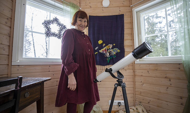 Nainen pienessä monikulmaisessa huoneessa kaukoputken kanssa.