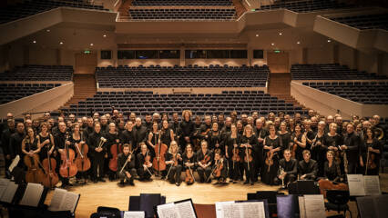 Tampere Filharmonia soi nyt sosiaalisessa mediassa. Filharmonian jäsenet poseeravat suuressa ryhmäkuvassa kameralle. Sali on muuten tyhjä ja sävyt ovat lämpimät.