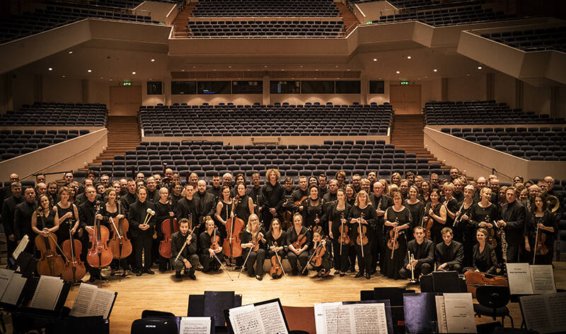 Tampere Filharmonia soi nyt sosiaalisessa mediassa. Filharmonian jäsenet poseeravat suuressa ryhmäkuvassa kameralle. Sali on muuten tyhjä ja sävyt ovat lämpimät.