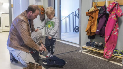 Mies riisuu lapsen kenkiä naulakon luona.