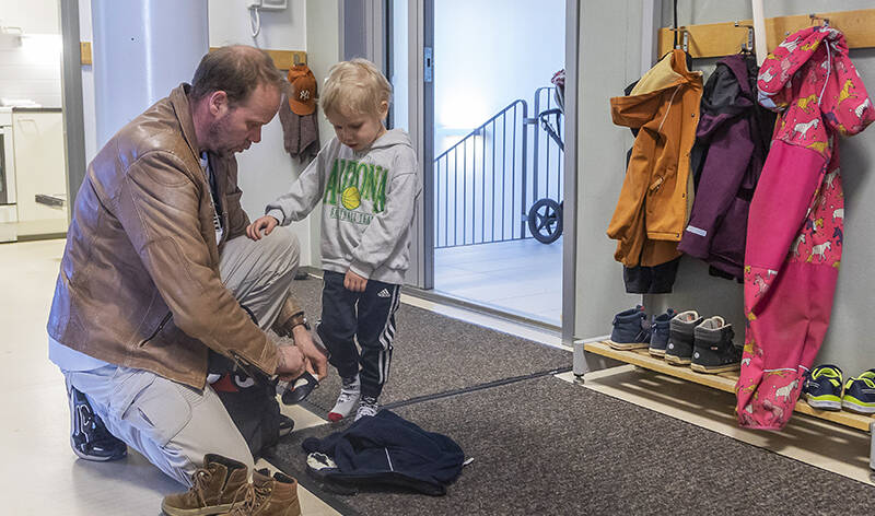 Mies riisuu lapsen kenkiä naulakon luona.