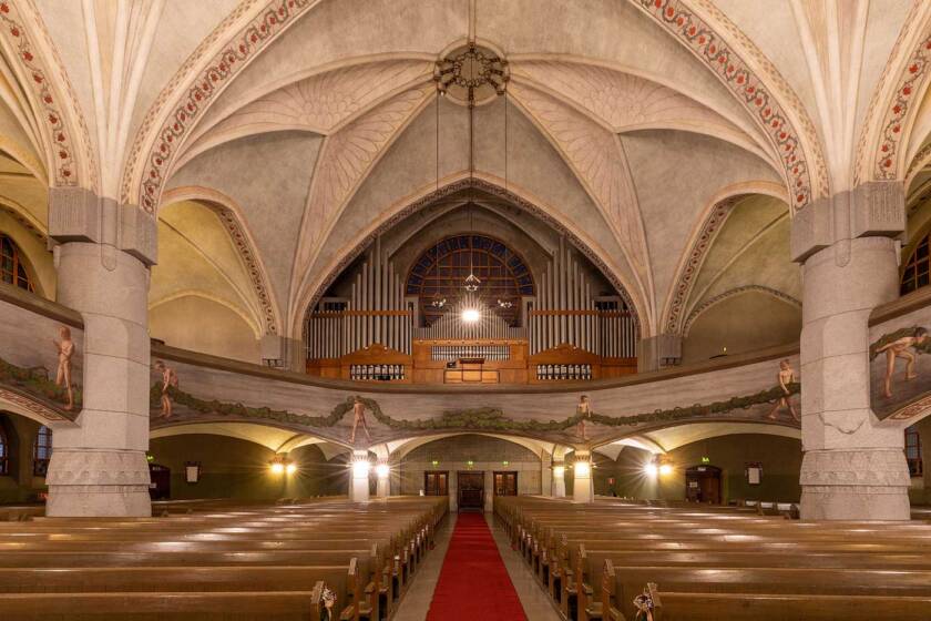 Interior of Tampere Cathedral seen from the central aisle, with rows of wooden pews, the vaulted ceiling and organ loft.