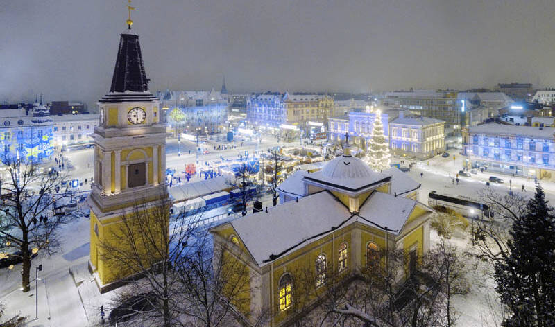 Vanha kirkko talvella yövalaistuksessa, taustalla joulutoria ja kaupungin joulukuusi.