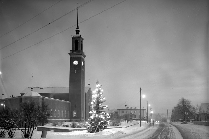 Mustavalkoin valokuva lumisesta kirkosta ja sen ympäristöstä.