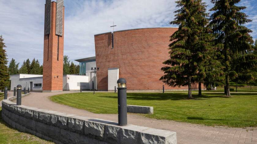 The general view of Aitolahti Church, showing a red brick bell tower and a curved wall of the church.