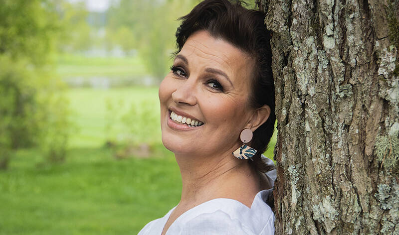 Laulaja Arja Koriseva nojaamassa puuhun.