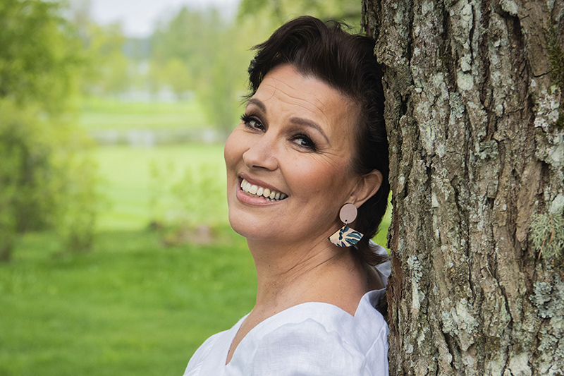 Laulaja Arja Koriseva nojaamassa puuhun.