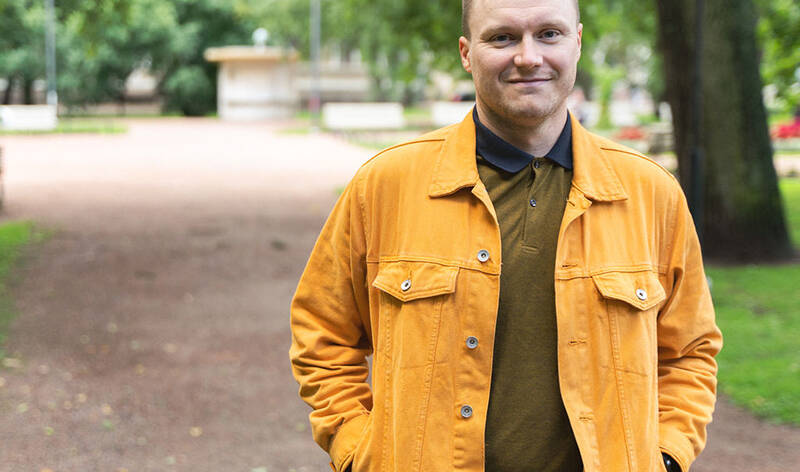Ylävartalokuva hymyilevästä miehestä vihreässä luonnossa.