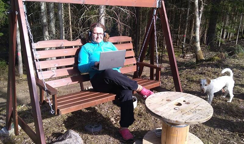 Diakoniatyöntekijä Hanna Kelokaski istuu pihakeinussa kuulokkeet päässä ja pitää kannettavaa tietokonetta sylissään.