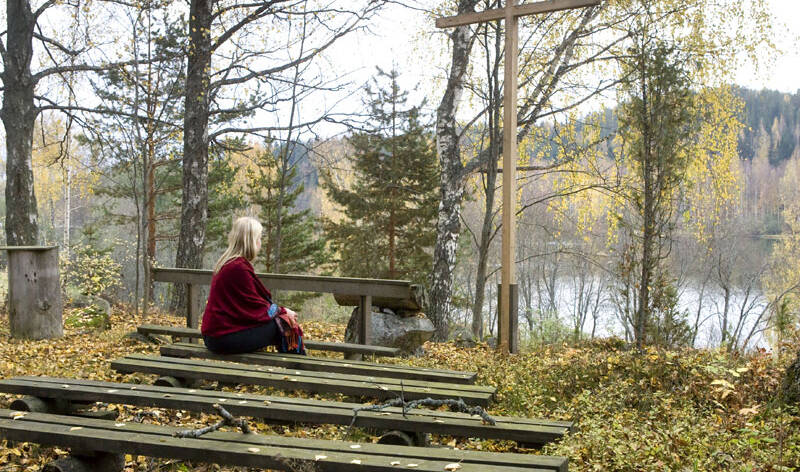 Nainen on hiljentynyt syksyisen metsäkirkon penkillä.