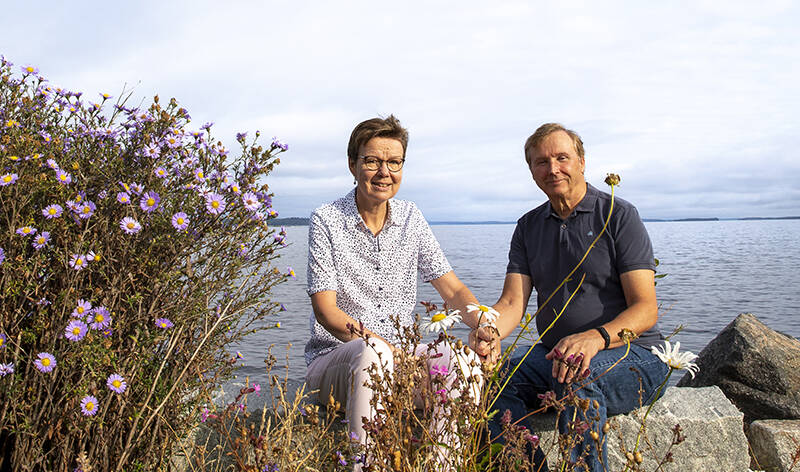 Pariskunta istuu käsikädessä rannan kalliolla.