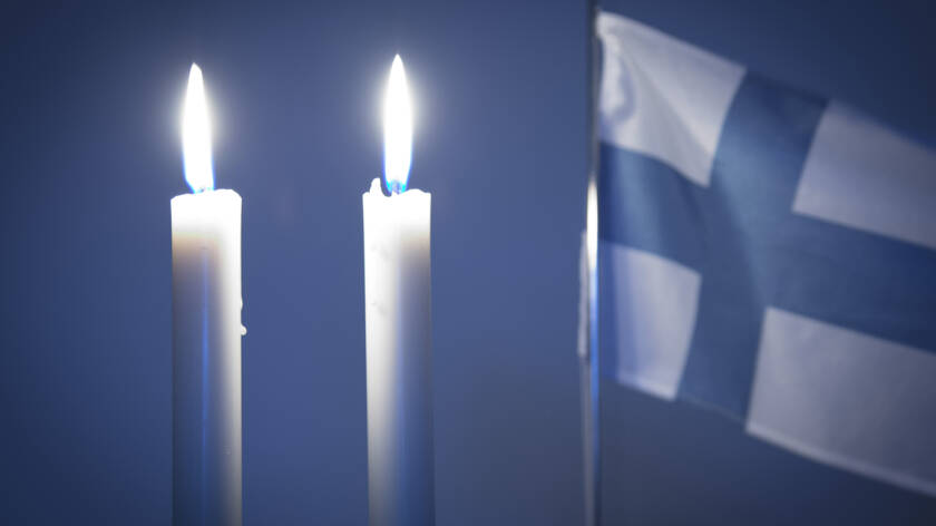 Kaksi kynttilää palaa ja suomen lippu liehuu taustalla.