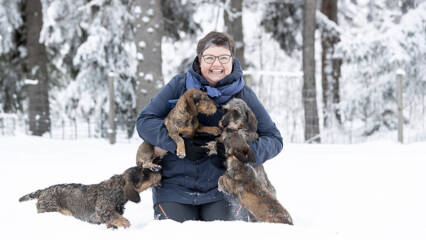 Iloinen nainen ja kolme koiraa lumihangessa.