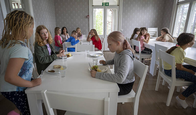 Lapset syövät pöydissä valoisassa salissa.