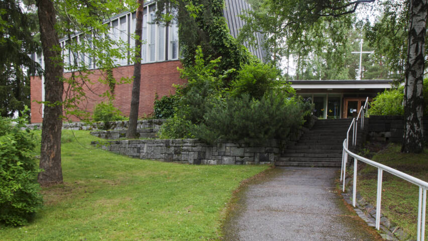 Lielahden kirkko on vehreiden puiden takana. Kirkolle johtaa polku nurmen halki.