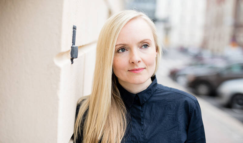 Vaalea nainen tummassa mekossa katsoo ylävasemmalle.