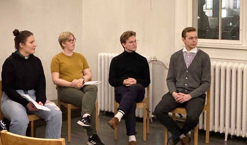Kaski naista ja kaksi miestä istuvat tuolilla ksisätilassa ikkunan edessä.
