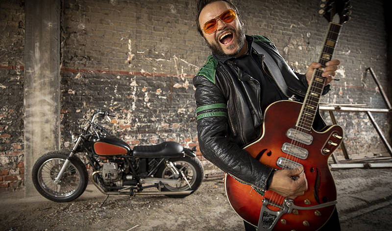 Oskari, alias Knucklebone Oscar, Martimo poseeraa sähkökitaran kanssa ränsistyneessä tehdasrakennuksessa. Mies hehkuu villiä rock-energiaa ja taustalle on pysäköity rakenneltu moottoripyörä. Yllään Oskarilla on rotsi, jossa on vihreitä raitoja sekä vihreät olkapäät, ja oranssit aurinkolasit.