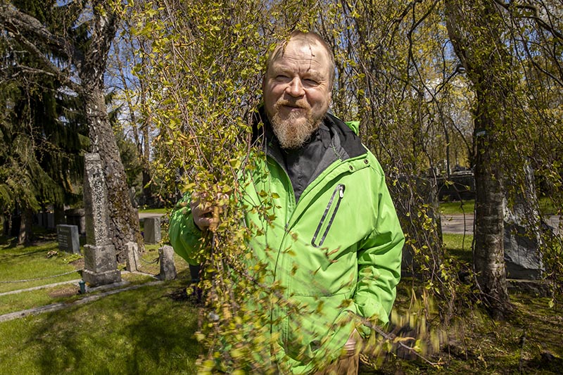 Partamies seisoo vihreässä takissa osittain puun oksan takana.