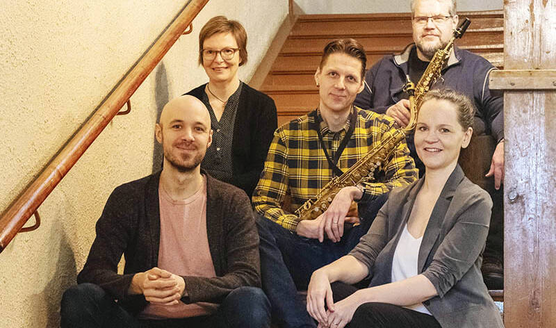 Kaksi naista ja kolme miestä istuu portailla, kahdella miehellä on saksofonit kädessä.
