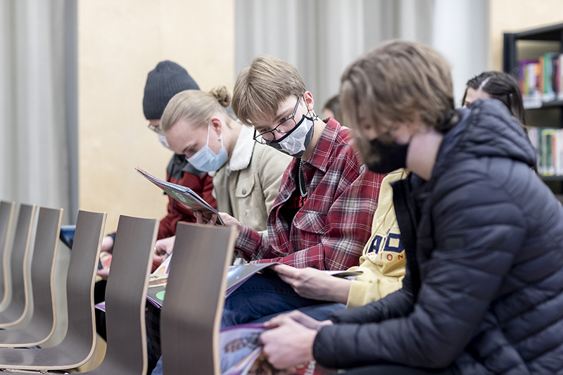 Lukiolaiset nuoret istuvat tuoleilla rivissä ja tutkivat Silta-lehteä. Kaikilla on maskit naamalla.