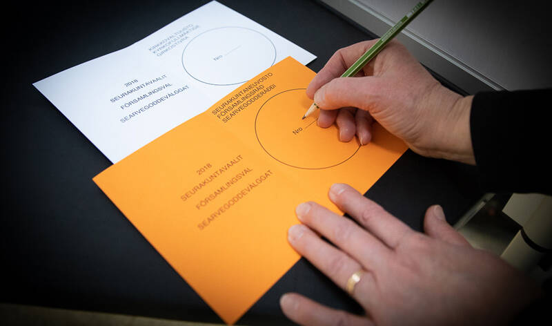 Pöydällä on valkoinen ja oranssi äänestyslippu, ja oranssiin lippuun kirjoitetaan.