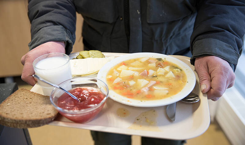 Kantavissa käsissä on tarjotin, jolla on keittolautanen, kiisseli, leipä ja maitolasi.